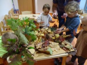 Trójka dzieci dotyka jesiennych liści wraz z opiekunem