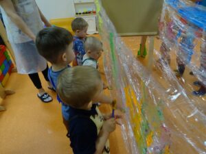 Dzieci stoją przy folii i malują farbami