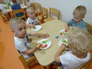Dzieci przy stoliku przyklejają owoce z kartki