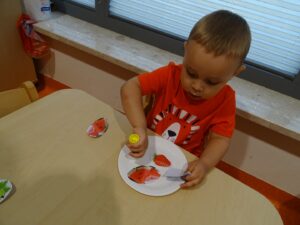 Dziecko siedzi i keli klejem owoce do talerza