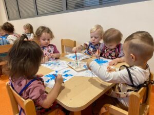 Dzieci siedzą przy stolikach i malują