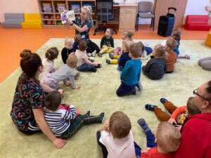 Dzieci siedza a dywanie a opiekunka czyta książke