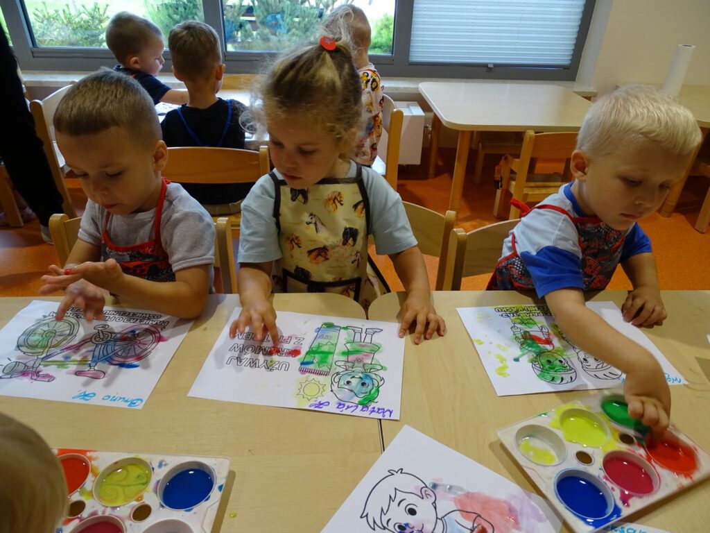 Dzieci przy stolikach malują farbami