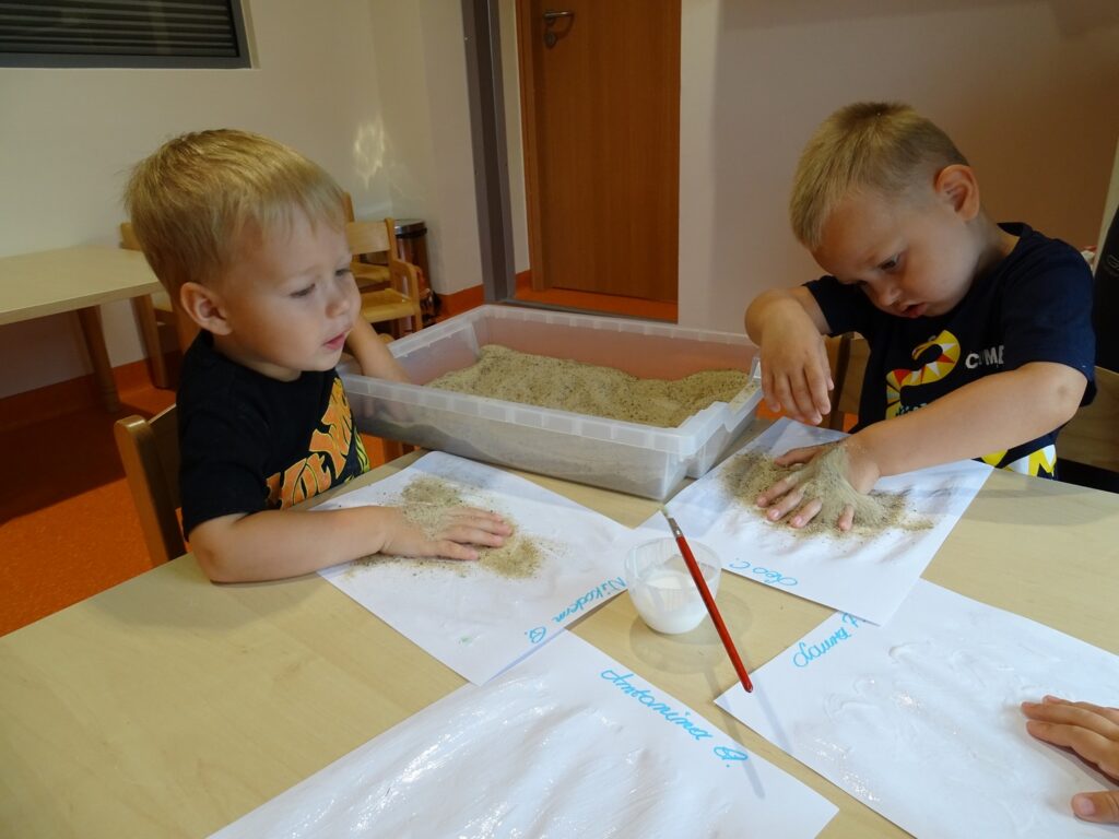 Chłopczyk sypie piasek na kartkę