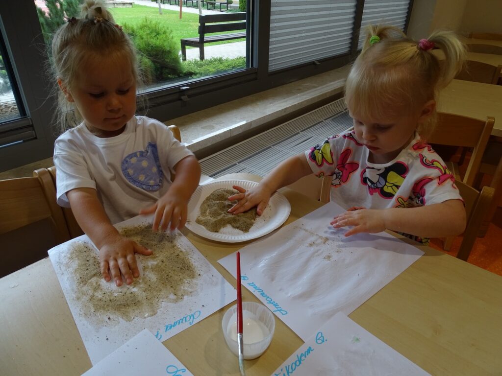 Dziewczynki sypią piasek na kartkę