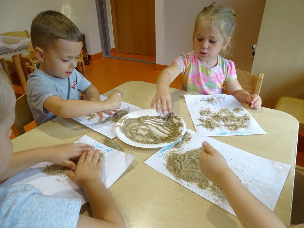 Dziewczynka z chłopcem sypie piasek na kartkę