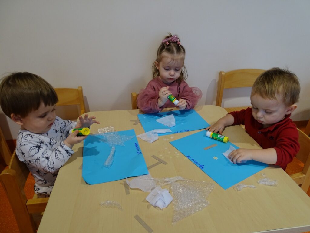 Dzieci przyklejają elementy na kartkę