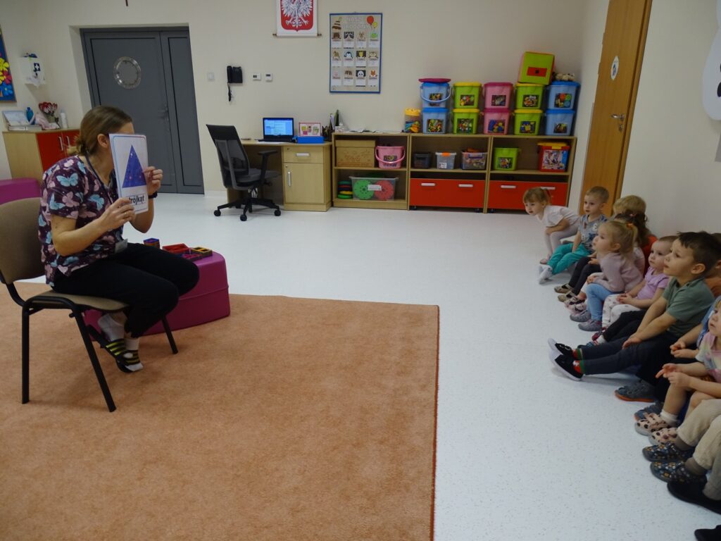 Opiekunka pokazuje dzieciom figury geometryczne