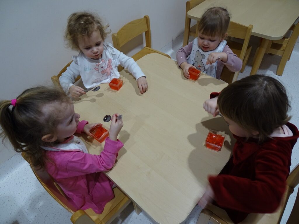 Dzieci przy stolikach jedzą galaretkę