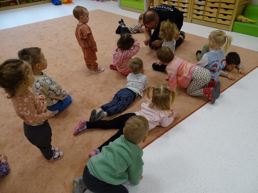 Dzieci kładą się na dywanie udając jajko dinozaura