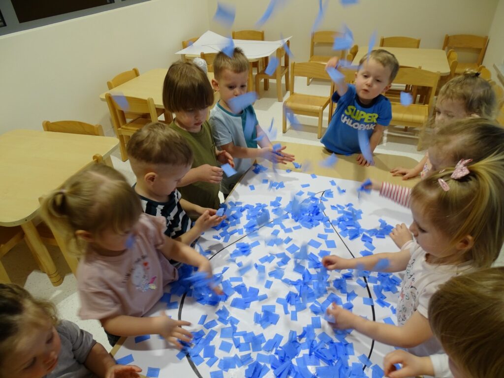 Dzieci wysypują na obrazek pocięte skrawki bibuły