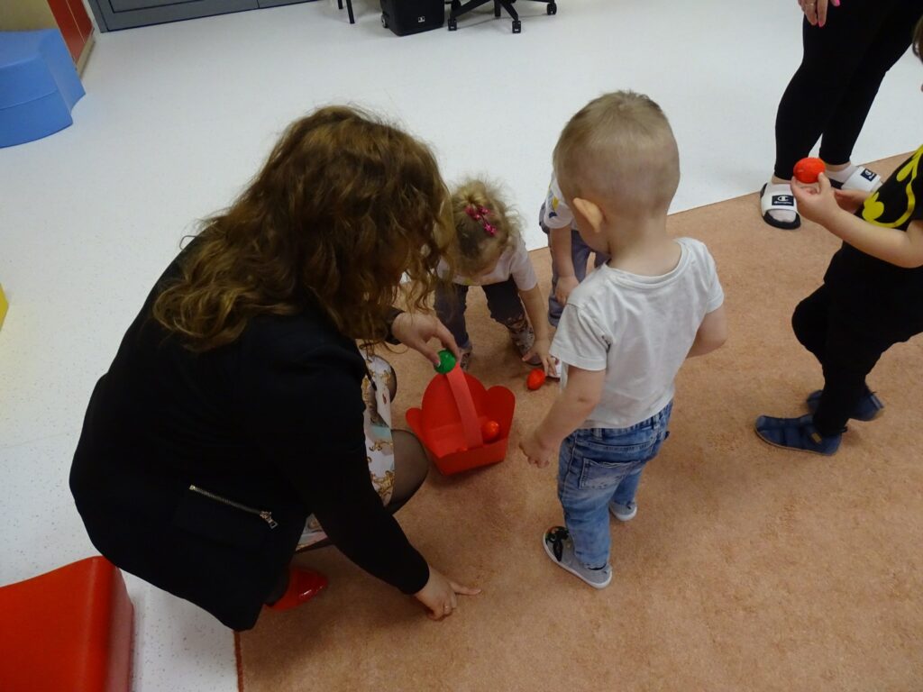 Chłopczyk wkłada czerwone jajeczko do koszyczka