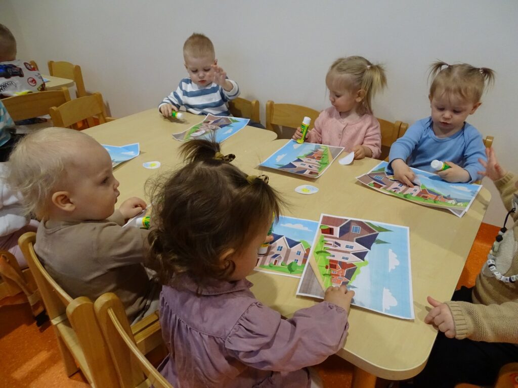 Dzieci siedzą przy stolikach i wykonują pracę plastyczną