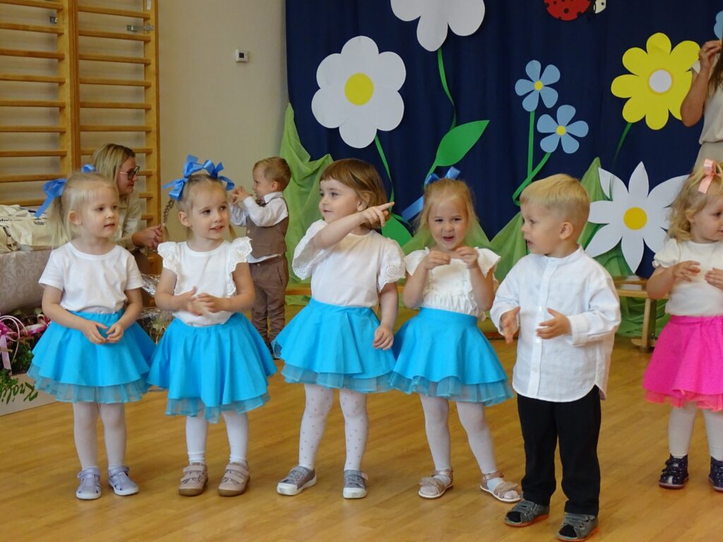 Dziewczynki w niebieskich spódniczkach tańczą wraz z chłopcem
