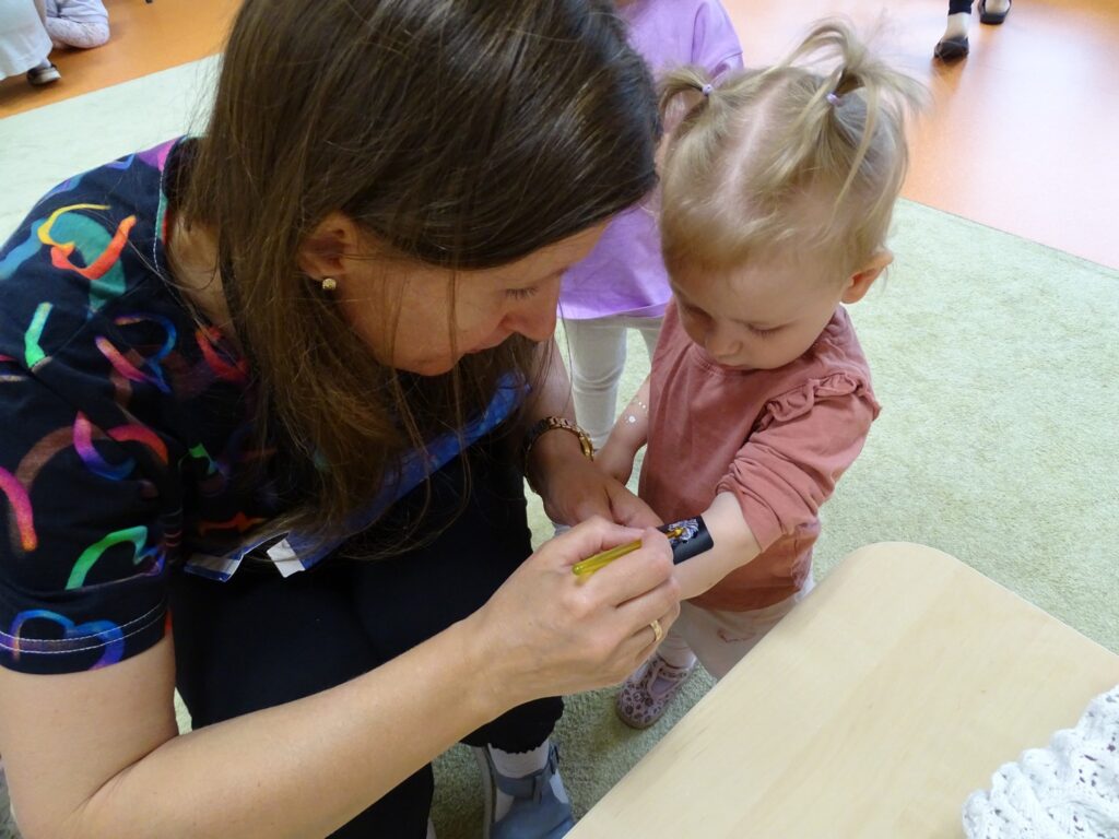 Pani przykleja dziewczynce brokatowy tatuaż